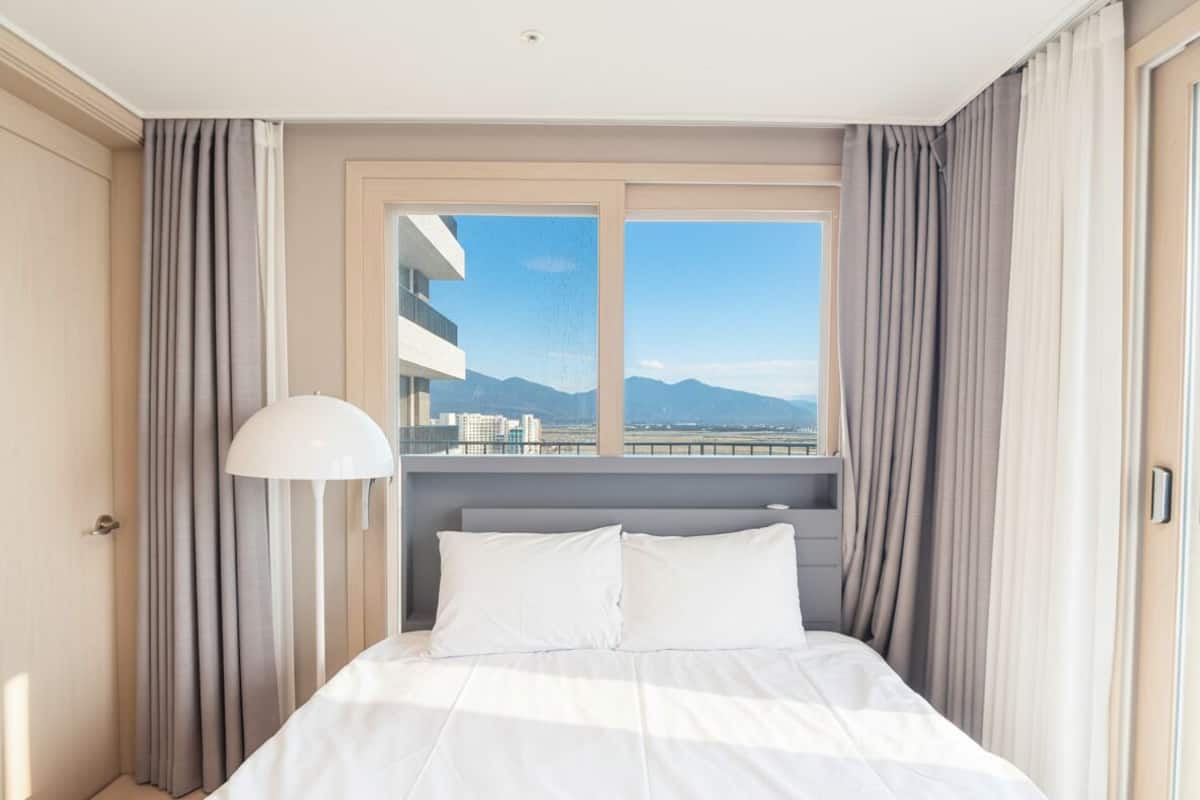Una habitación de hotel con cama, lámpara y ventana con cortinas.