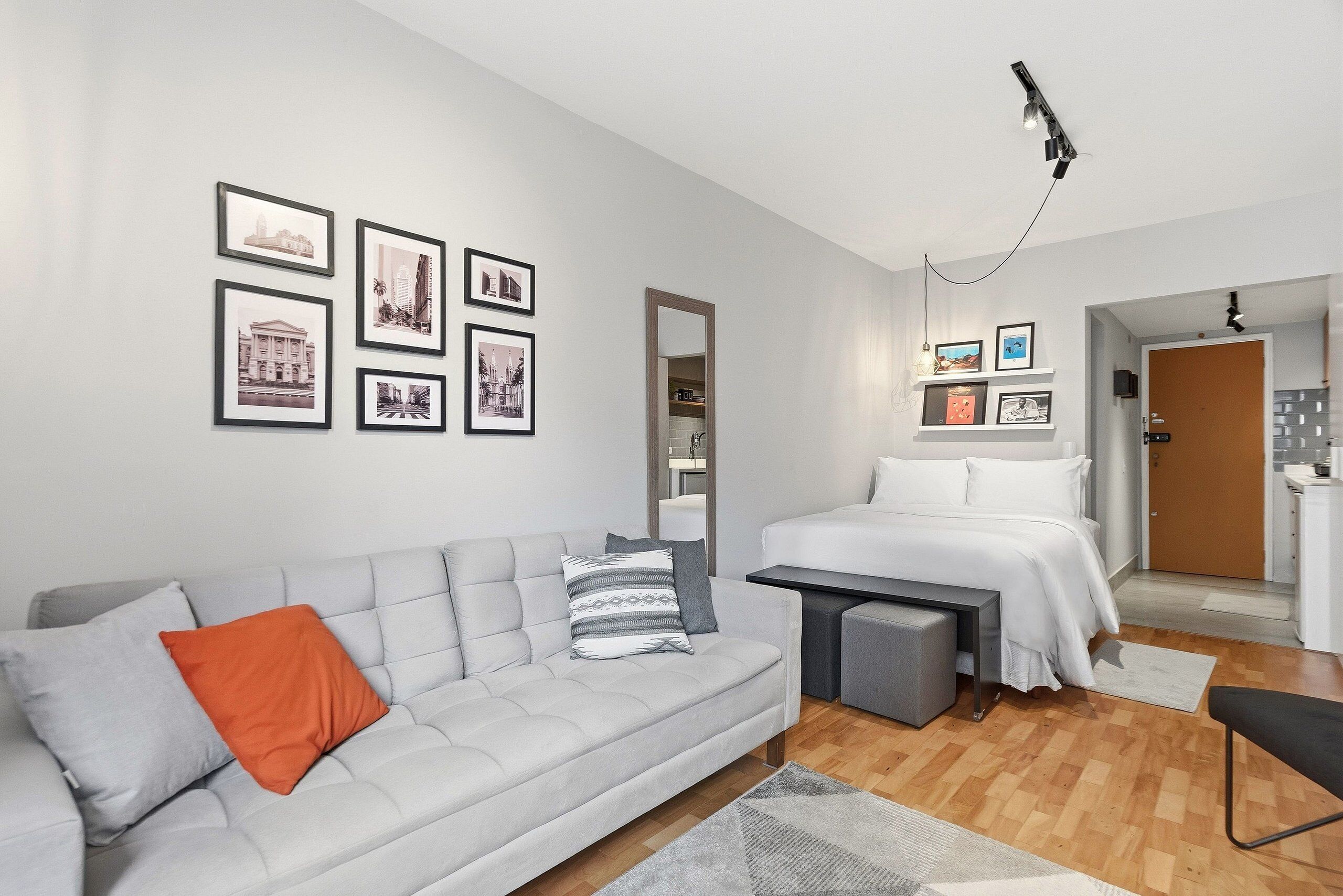 Un dormitorio moderno con un sofá gris, una cama, una mesita de noche, un espejo y cuadros enmarcados en la pared.