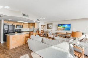 Eine moderne Küche mit Kochinsel, Holzschränken und einem Essbereich mit Sofa und Lampe.