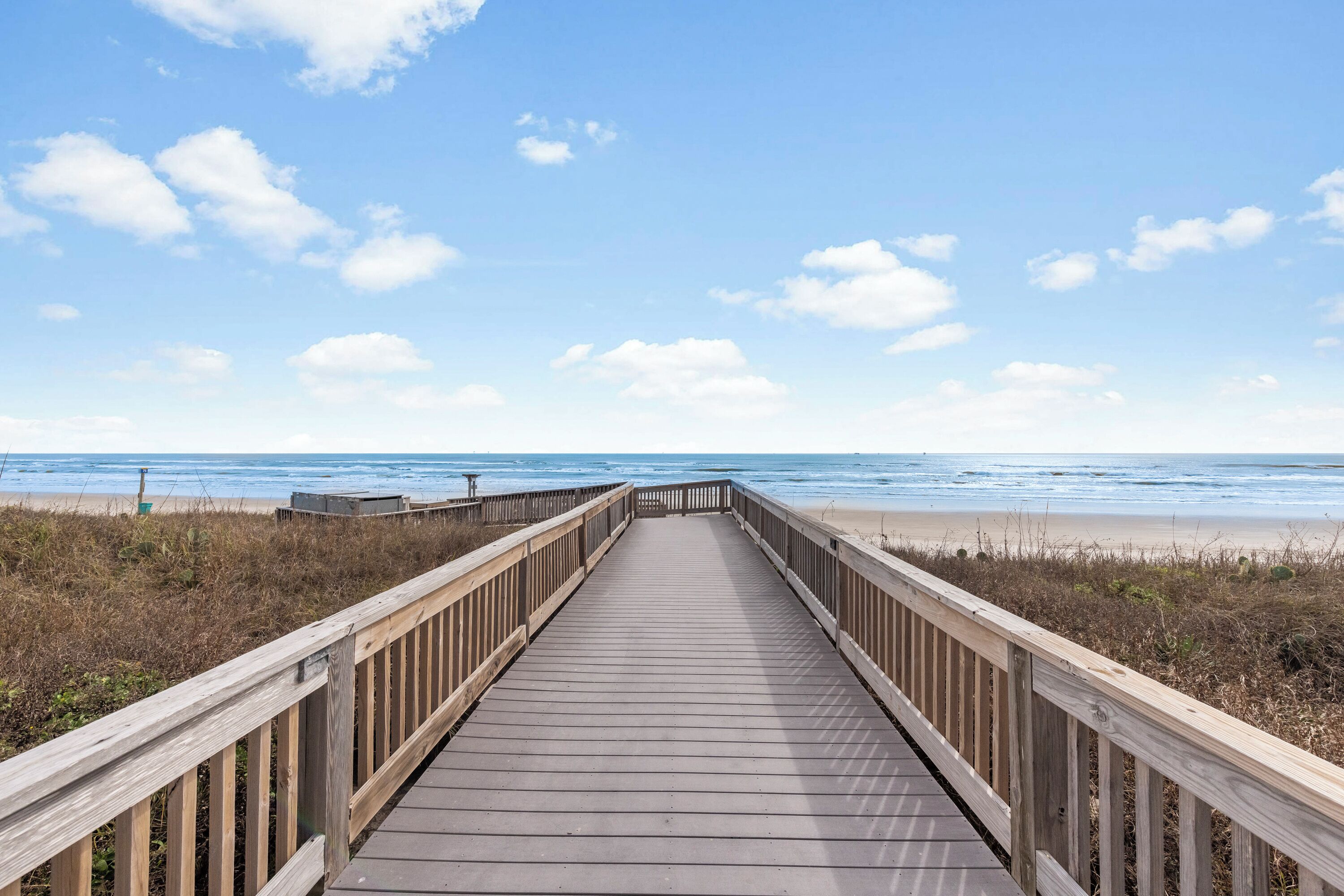 A wooden boardwalk leading to a beach with a clear sky.