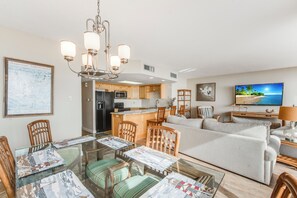 Ein modernes Wohnzimmer mit Glastisch, Holzkreisen, einer Couch und einer Küchenzeile, sowie einem Fernseher.