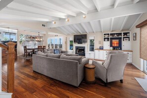 Ein geräumiger Wohnbereich mit einer Couch, Sesseln, einem Kamin und einer Küche mit Fernseher.