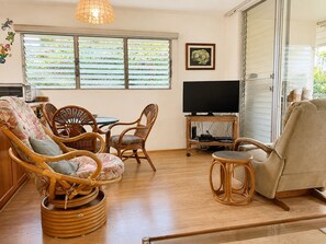Ein Wohnzimmer mit Rattanmöbeln, einem Fernseher und einem Fenster mit Jalousien.