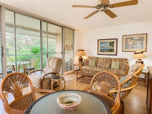 A living room with wicker furniture, a ceiling fan, and large windows. - Soothing condo in Kihei perfect for relaxing stays (Kihei)