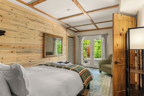 Ein Zimmer mit Holzwänden, einem Bett, einem Sessel und einer Tür.