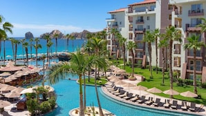 Een resort met een groot zwembad, palmbomen en uitzicht op de oceaan.