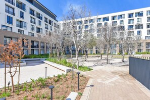 Un bâtiment moderne à plusieurs étages, doté d’espaces de détente en plein air et d’une cour aménagée avec des arbres et des plantes.