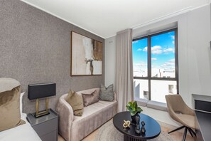 Ein modernes Hotelzimmer mit einer Couch, einem kleinen Tisch mit Pflanze, einem Nachttisch mit Lampe und einem großen Fenster mit Blick auf die Stadt.