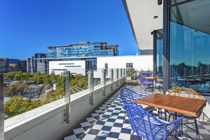Eine Dachterrasse mit Schachbrettboden, blauen Stühlen und einem Holztisch.