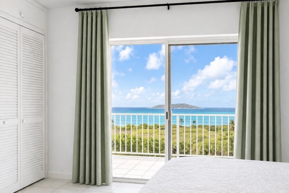 Een slaapkamer met een groot bed, een schuifdeur naar een balkon met uitzicht op de oceaan en een eiland in de verte.