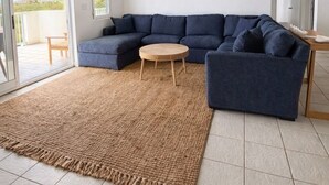Olohuoneessa on kulmasohva, pyöreä sohvapöytä, kattotuuletin ja suuri ikkuna, josta on kaunis näkymä.