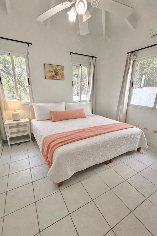 A bedroom with a bed, a nightstand, a ceiling fan, and windows.