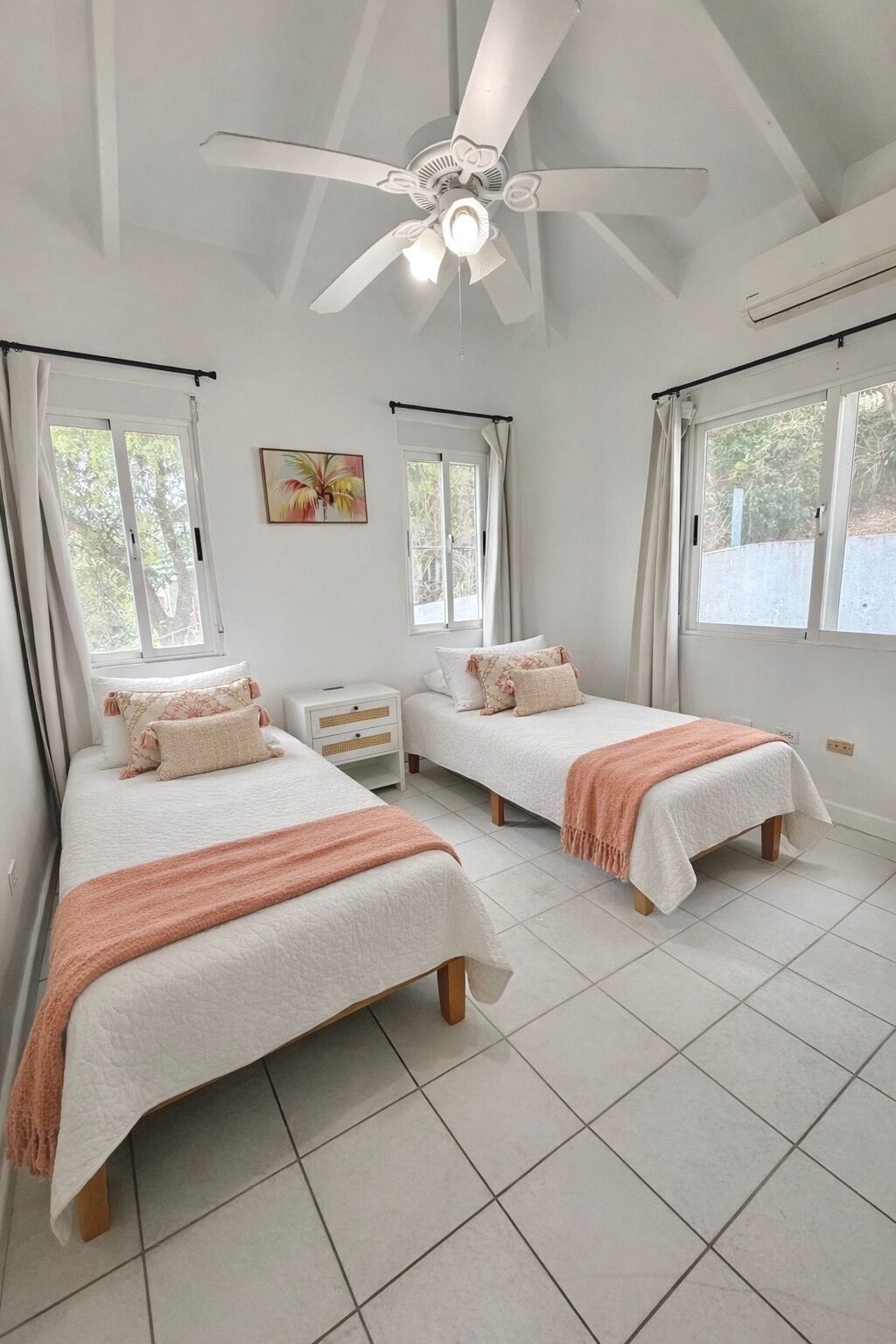 Dormitorio con dos camas, ventilador de techo y ventanas amplias.