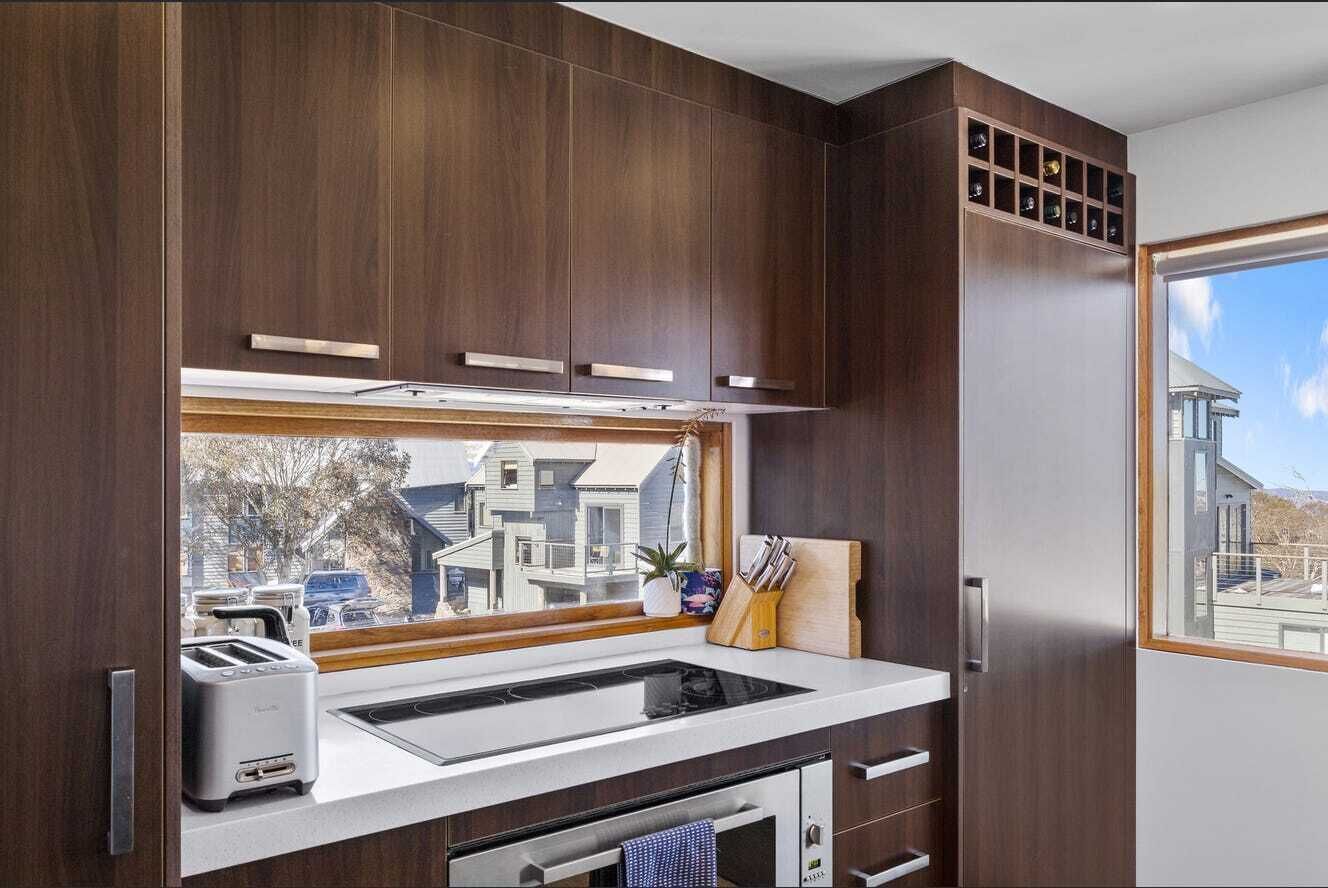 Une cuisine compacte avec une fenêtre, des appareils électroménagers intégrés et une vue sur le quartier.