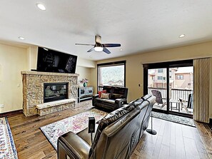 A living room with a stone fireplace, leather sofa, and a large window overlooking a balcony. - Alders Haven w/Priv Hot Tub, Access to Slopes (Keystone)