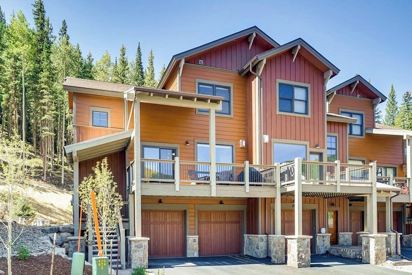 A multi-story wooden building with a balcony, garage doors, and a stone foundation.