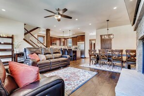 A spacious living room with a leather sofa, a dining area with wooden chairs, a kitchen in the background, and a staircase leading to an upper level. - Alders Haven w/Priv Hot Tub, Access to Slopes (Keystone)