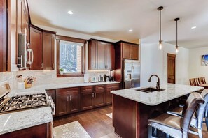 A kitchen with wooden cabinets, a granite countertop, a stainless steel refrigerator, and a built-in island with a sink. - Alders Haven w/Priv Hot Tub, Access to Slopes (Keystone)