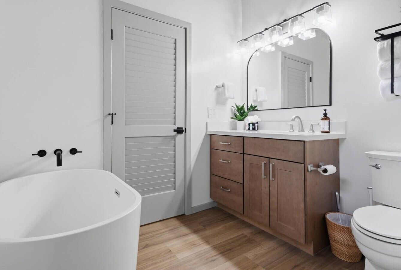 A bathroom with a bathtub, a toilet, a sink with a mirror, and wooden cabinets.