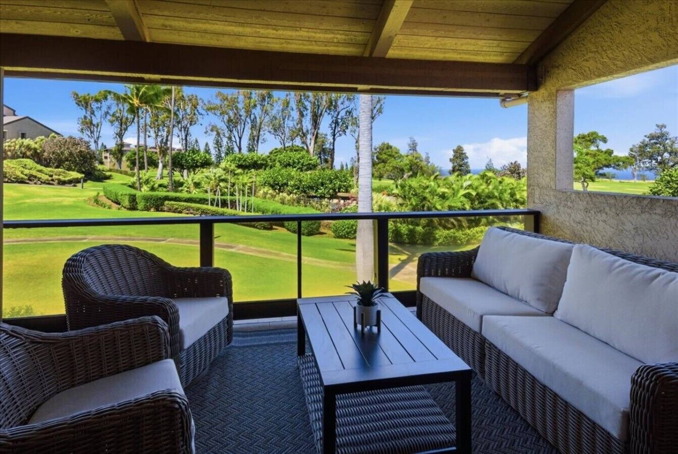 A balcony with wicker furniture, a small table, and a view of a golf course.