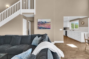 Ein Wohnzimmer mit einem dunkelgrauen Sofa, einer weißen Tagesdecke und einem Landschaftsbild.