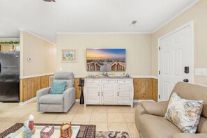 Ein Wohnzimmer mit einem beigen Sofa, einem grauen Sessel, einer weißen Kommode und einem Bild mit Strandmotiv.