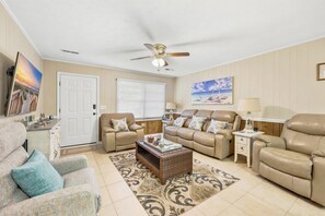 Ein Wohnzimmer mit beige gefärbten Wänden, einem Deckenventilator, einem Couchtisch, zwei Sofas, einem Beistelltisch und einer Tür.