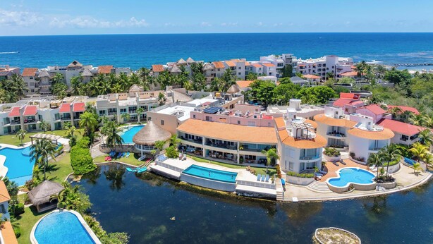 Un resort con varias edificaciones, una piscina central y vistas al océano.