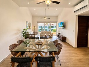 A spacious living area with a glass dining table, wicker chairs, a sofa, and a TV mounted on the wall. - Boutique Tropical Escape | Pool + Beach (Puerto Aventuras)