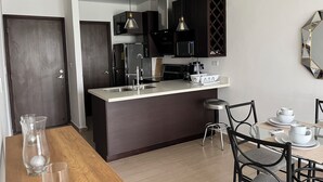 Une cuisine moderne dotée d’un îlot central, de meubles de rangement aux couleurs sombres et d’un coin repas avec une table et des chaises.