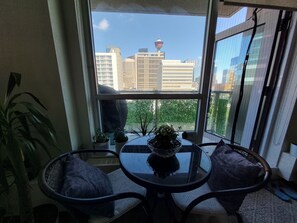 Ein Zimmer mit Blick auf eine Stadtlandschaft durch ein großes Fenster, ein runder Tisch mit Stühlen und Topfpflanzen.