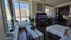 Quarto de hotel moderno com uma janela grande, televisão de tela plana, cama, escrivaninha e área de estar.