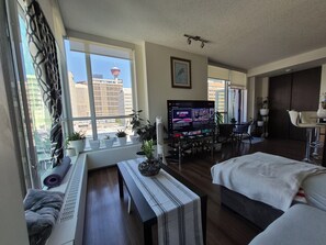 Ein modernes Hotelzimmer mit großem Fenster, Flachbildfernseher, Bett, Schreibtisch und Sitzecke.