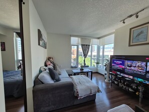 Ein Wohnzimmer mit einer Couch, einem Fernseher und einem Fenster mit Vorhängen.