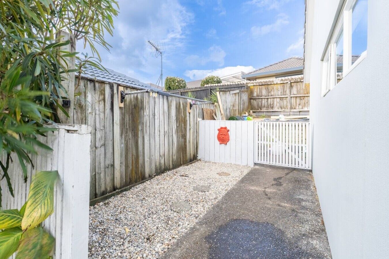A fenced outdoor area with gravel ground, a wooden fence, and a white wall.