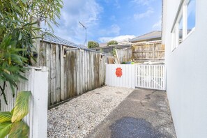 A fenced outdoor area with gravel ground, a wooden fence, and a white wall. - Comfortable 3-Bedroom Home in East Tamaki Heights (East Tamaki Heights)