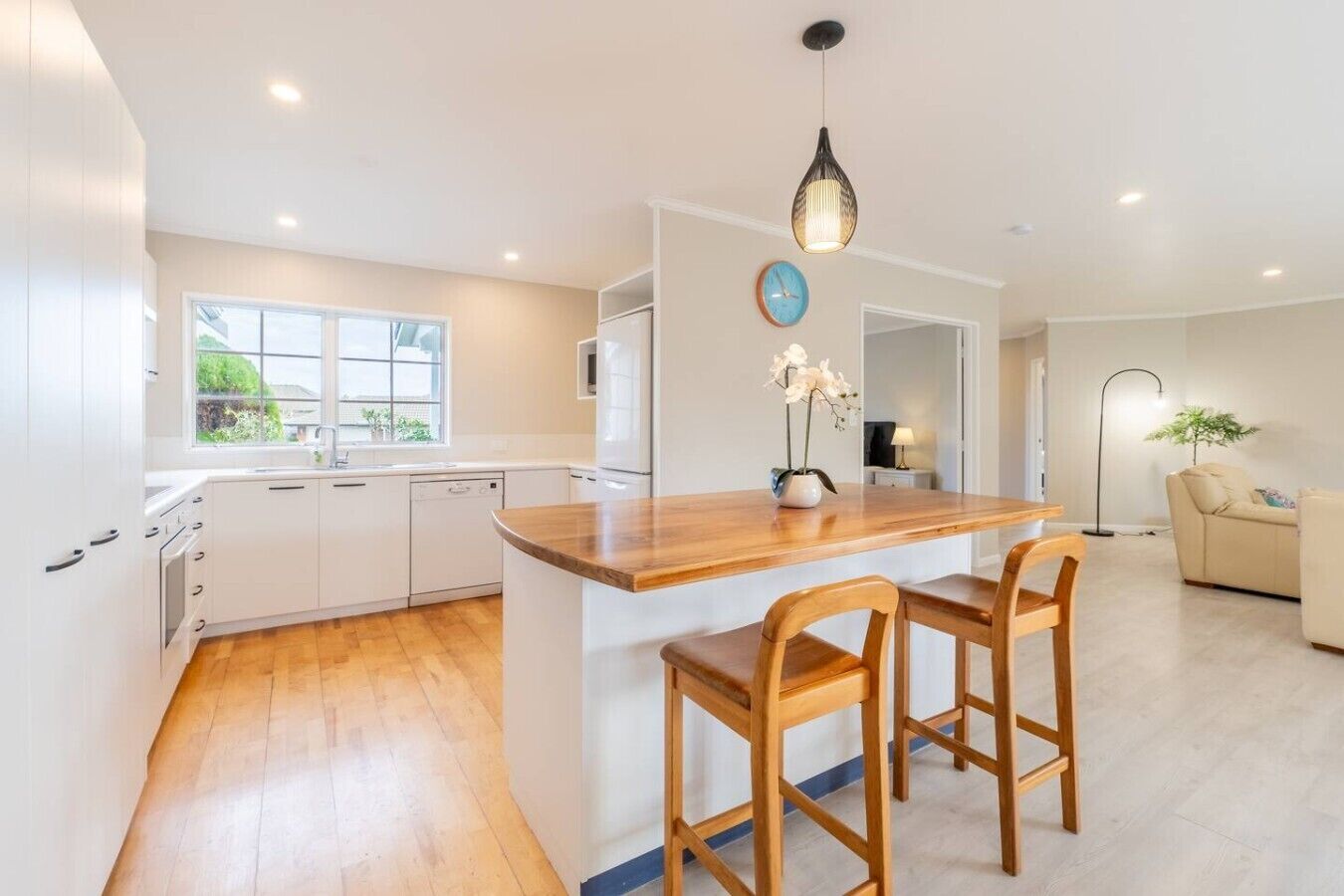 A modern kitchen with white cabinets, a wooden island with bar stools, a built-in oven, and a window providing natural light.