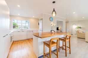 A modern kitchen with white cabinets, a wooden island with bar stools, a built-in oven, and a window providing natural light.