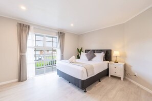 A bedroom with a bed, bedside table, lamp, curtains, and a view of the outside. - Comfortable 3-Bedroom Home in East Tamaki Heights (East Tamaki Heights)
