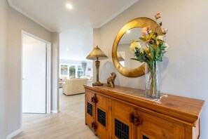A hallway with a wooden console, a mirror, and a vase with flowers. - Comfortable 3-Bedroom Home in East Tamaki Heights (East Tamaki Heights)