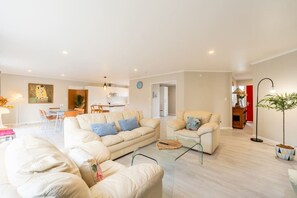A modern living room with a sofa, armchairs, and a coffee table. There is a dining area in the background with a table and chairs. - Comfortable 3-Bedroom Home in East Tamaki Heights (East Tamaki Heights)