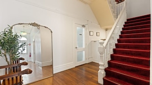 Un escalier recouvert d’une moquette rouge, avec une main courante en bois et une porte blanche dotée de panneaux en verre dépoli.