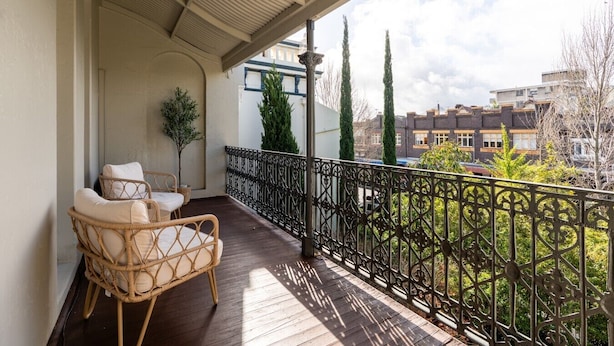 Un balcon avec un fauteuil en osier, une petite plante en pot et une rambarde en métal.
