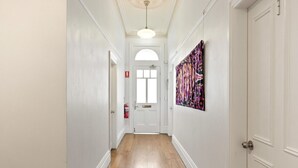 Un couloir aux murs blancs, au plancher en bois et au plafond orné de moulures décoratives.