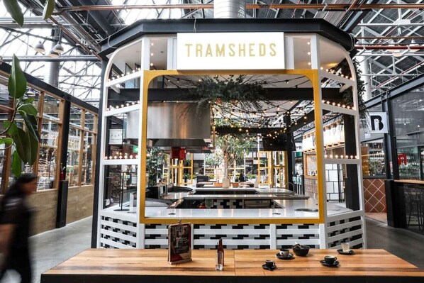 A restaurant named TRAMSHEDS with a modern interior, a central cooking area, and a view of the surrounding mall. - Grand Victorian Stay in the Heart of Glebe (Glebe)