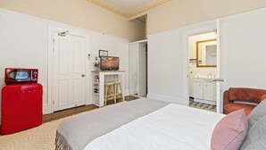 Una camera da letto con un letto, un elettrodomestico rosso, una televisione e un bagno parzialmente visibile attraverso una porta aperta.