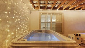 Uma banheira de hidromassagem em um quarto com parede texturizada, janela com persianas e teto de madeira.