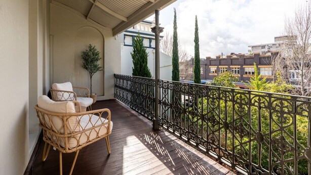 A balcony with a wicker chair, a small potted plant, and a metal railing. - Grand Victorian Stay in the Heart of Glebe (Glebe)