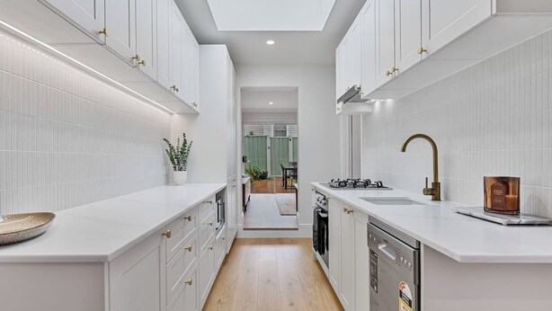 A modern kitchen with white cabinetry, a skylight, and a view into the dining area.