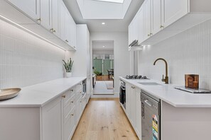 A modern kitchen with white cabinetry, a skylight, and a view into the dining area. - Charming Sunlit Terrace in Vibrant Newtown (Newtown)